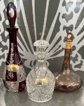 A group of three assorted glass decanters comprising a clear and ruby cut glass decanter and