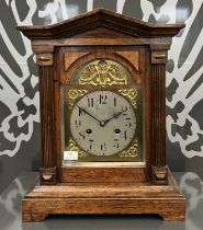 An early 20th century oak architectural form mantle clock, the brass arched dial with silvered