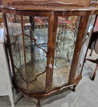 An early 20th century serpentine front display cabinet, the central glazed panel with chromed mirror