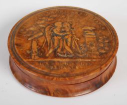 A treen circular snuff box, the pressed wood detachable cover depicting embracing classical