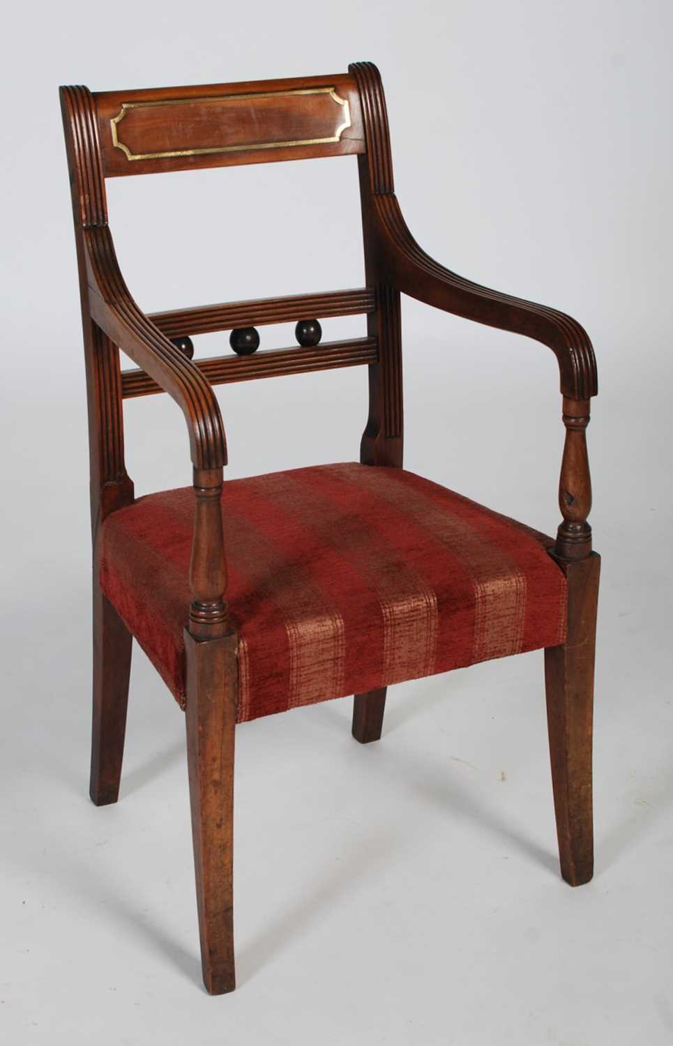 An early 19th century walnut and brass inlaid childs elbow chair, the rectangular top rail with