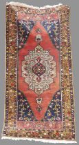 A Turkish long rug, 20th century, the rectangular abrashed madder ground centred with a large oval