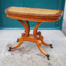 A 19th century satinwood and yew wood tea table, the hinged demi-line top raised on four scroll