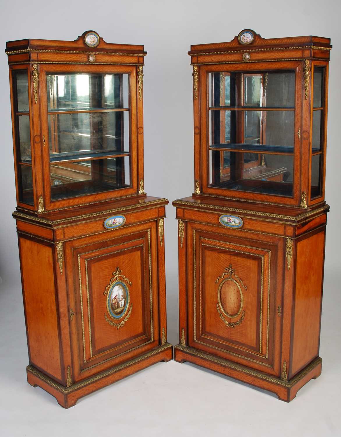 A pair of late 19th century satinwood, porcelain and gilt metal mounted display cabinets, the