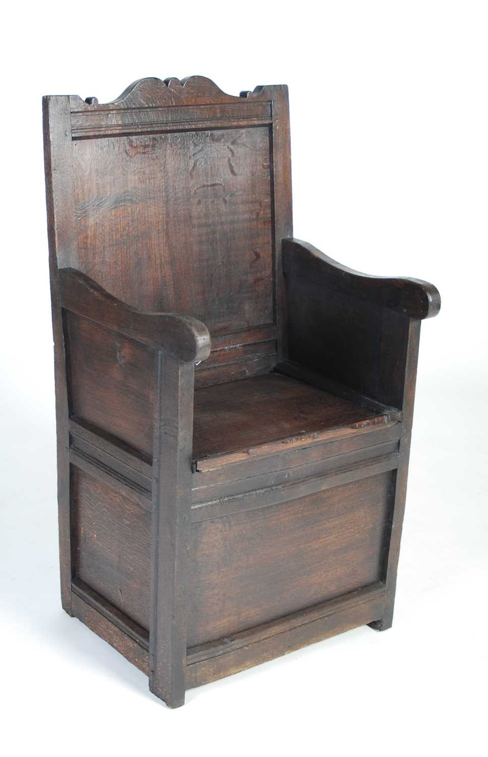 An 18th century oak lambing chair, the shaped top rail above a rectangular panelled back, the box