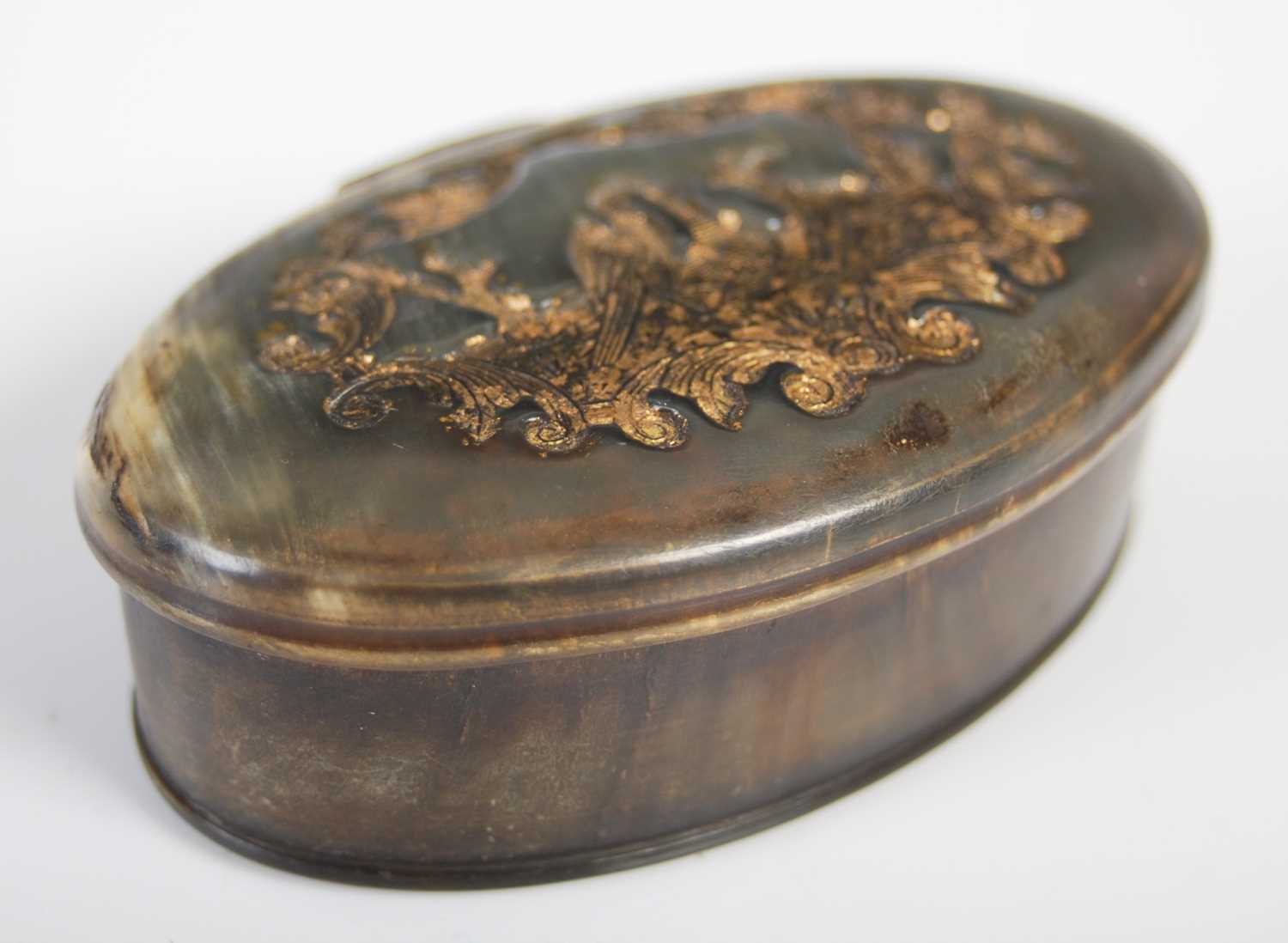 A pressed horn oval snuff box, the hinged cover decorated with a pelican, basket and dog within