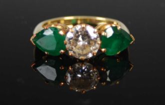 An 18ct gold, emerald and diamond three stone ring, centred with a round brilliant cut diamond