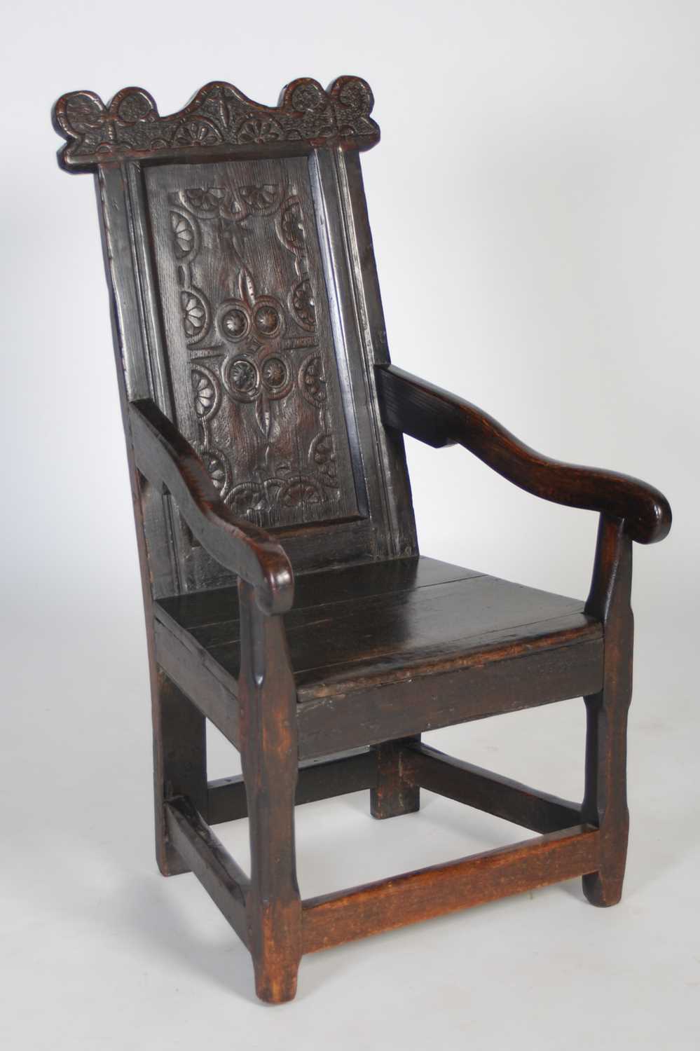 An 18th century oak wainscot elbow chair, the shaped top rail carved with two demi-lune stylised