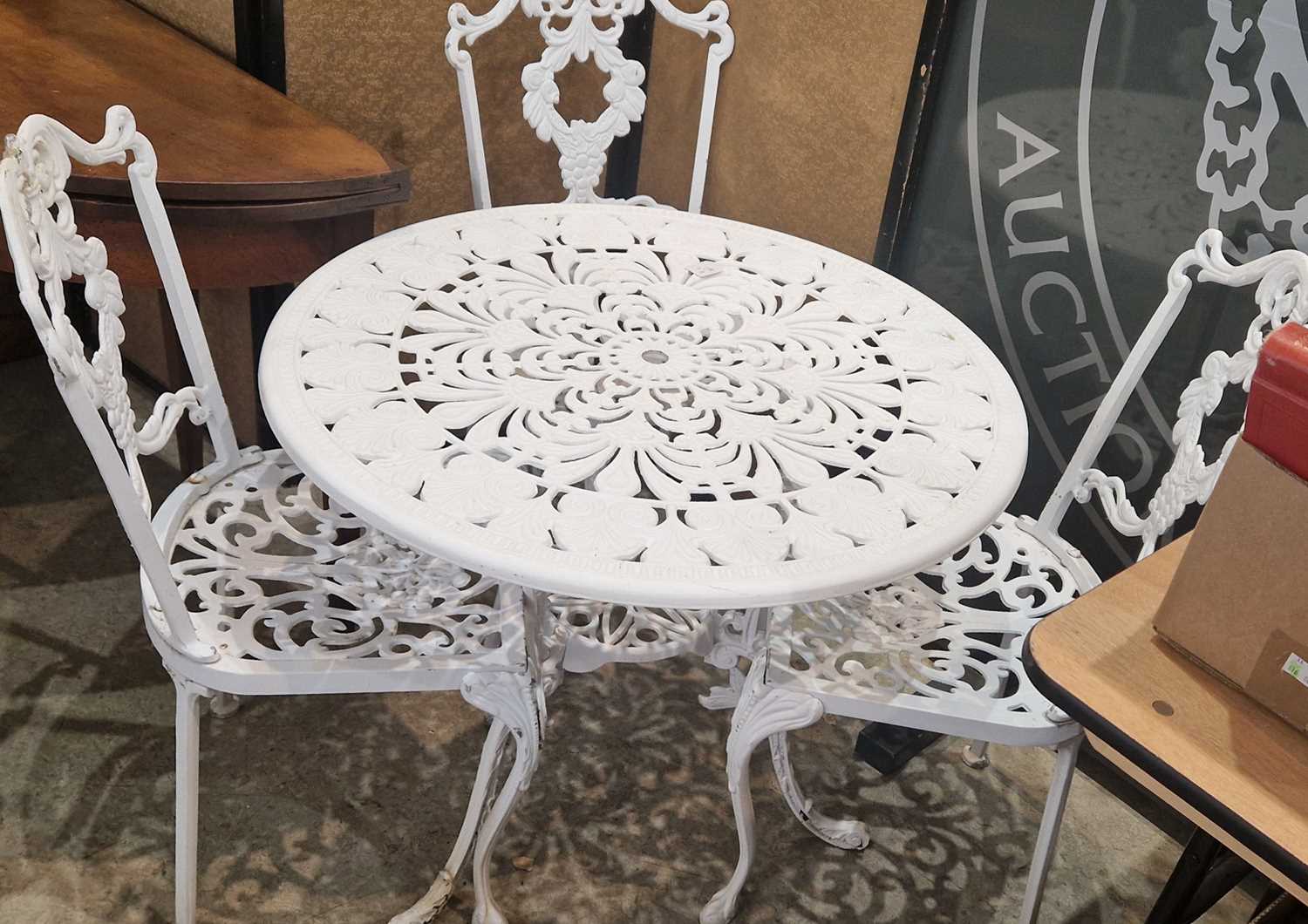 A white-painted cast metal garden table and three chairs, the table 81cm diameter.