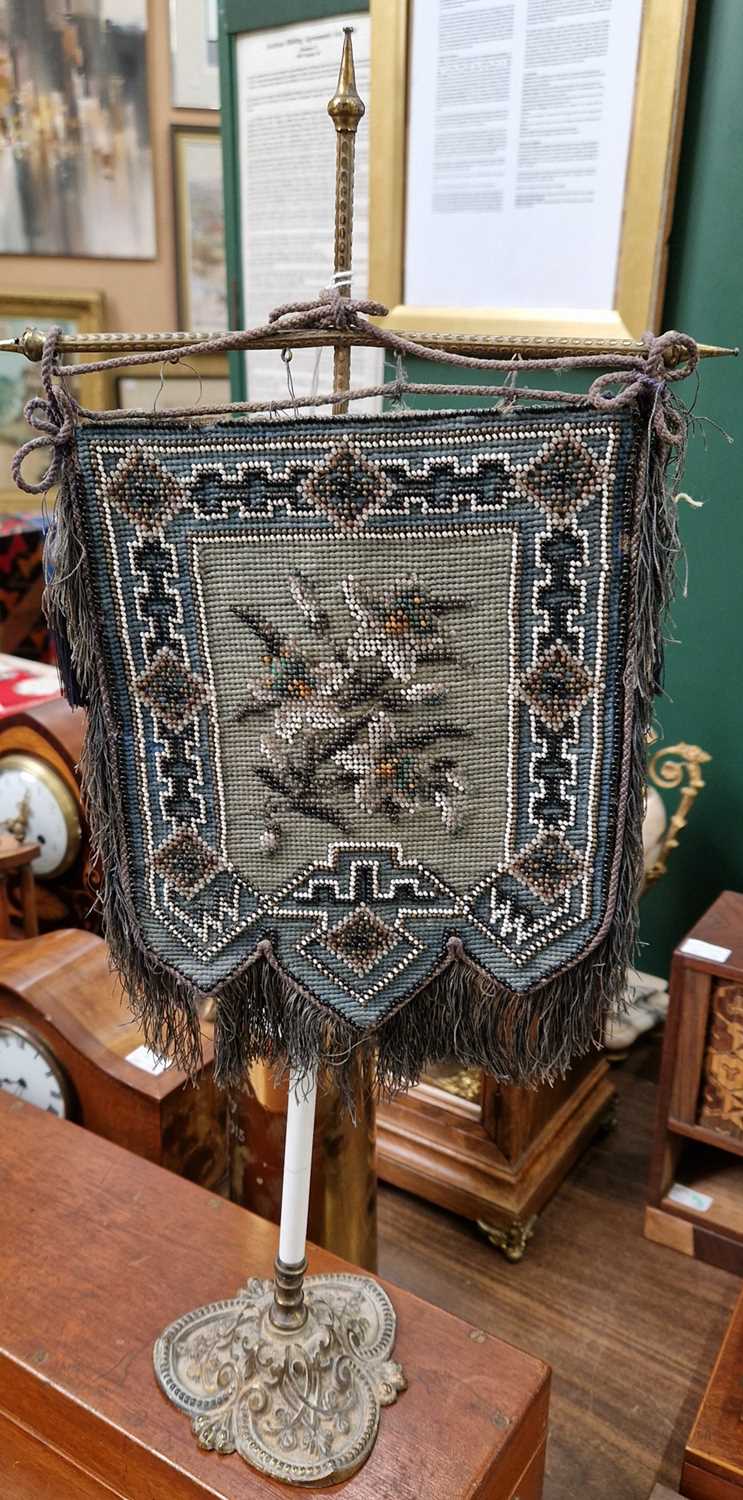 An antique beadwork table screen centered with floral detail surrounded by a stylised border with