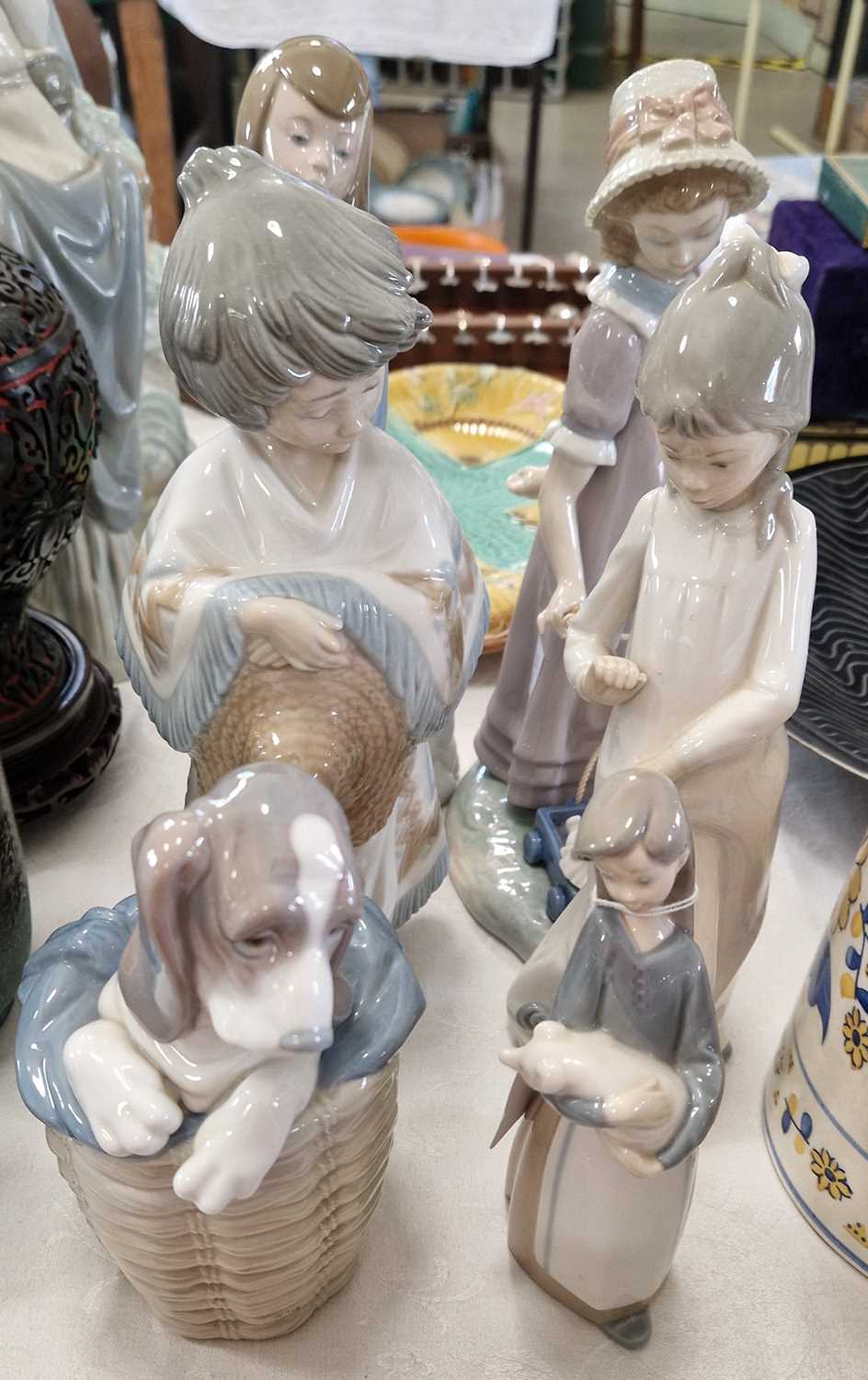 Three Lladro figures to include a girl holding a dog, a dog in a basket and a girl pulling a dolly