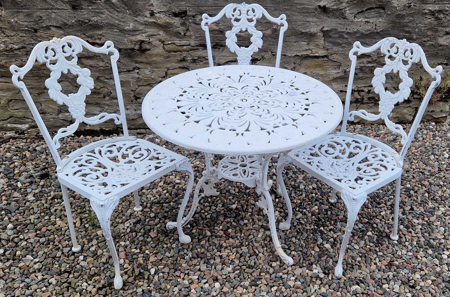 A white-painted cast metal garden table and three chairs, the table 81cm diameter.