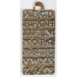 An antique brass alphabet plaque teaching aid, the reverse inscribed 'St. Pauls AD1729', cast in