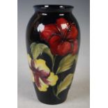 A Moorcroft pottery vase decorated with hibiscus on a dark blue ground, 18cm high.