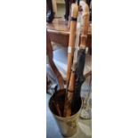 A brass stick stand, containing two umbrellas, a walking cane and a shoehorn.