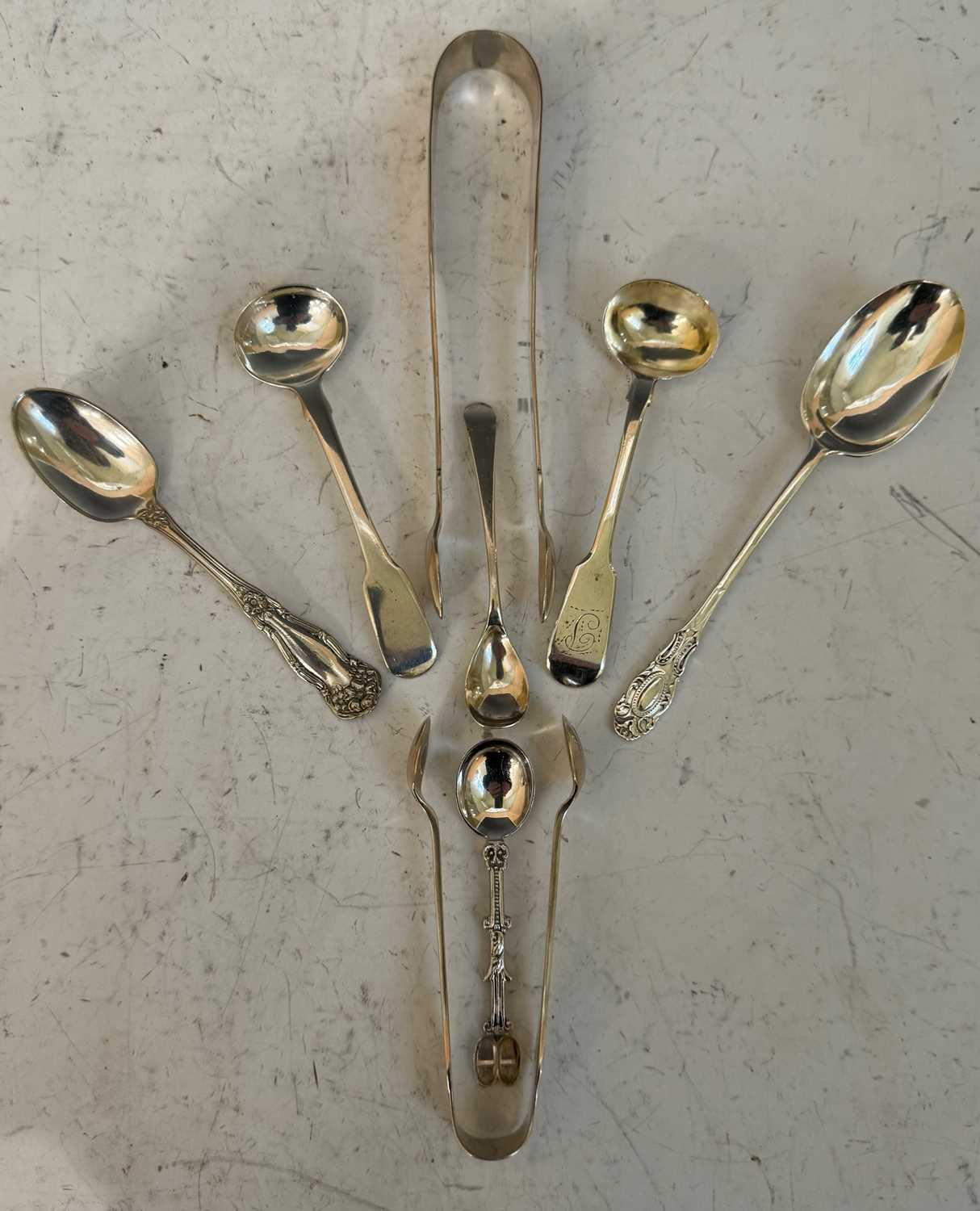 A collection of assorted silver flatware to include two pairs of sugar tongs, mustard salt and