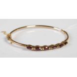 A 9ct gold and garnet six stone hinged bangle, gross weight 6 grams.