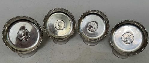 Four assorted white metal coin set dishes, each inscribed silver, two set with Victorian coins,