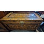A Chinese camphor wood blanket box, carved with panels of figures raised on four claw shaped feet,