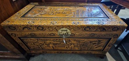 A Chinese camphor wood blanket box, carved with panels of figures raised on four claw shaped feet,