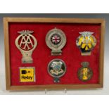 Automotive interest - A montage of six assorted car badges, mounted in a wooden frame with red baize