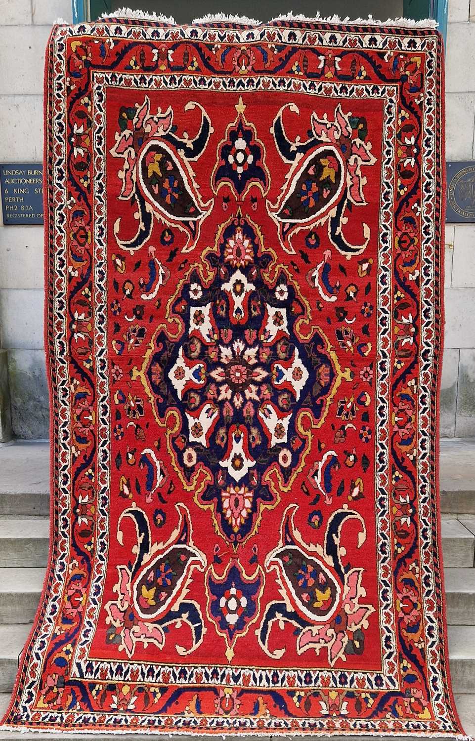 A Persian rug, 20th century, the rectangular madder ground centered with a blue ground oval