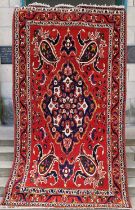 A Persian rug, 20th century, the rectangular madder ground centered with a blue ground oval