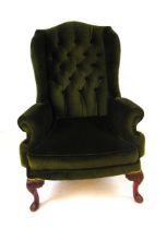 A George III style upholstered wing armchair, with button back and scroll armrests, on short foliate