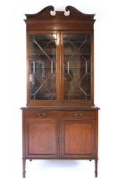An Edwardian mahogany and inlaid strung bookcase on cupboard, with swans neck pediment over astragal