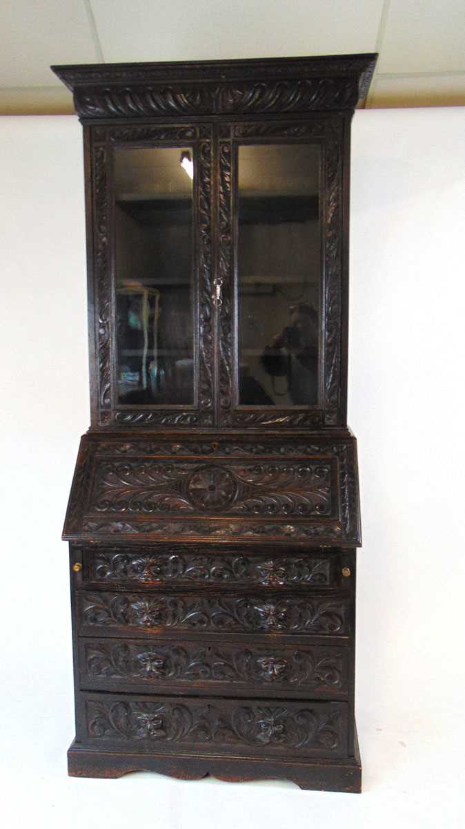 A late Victorian carved and ebonised oak bureau bookcase, the glazed doors enclosing adjustable