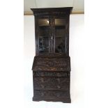 A late Victorian carved and ebonised oak bureau bookcase, the glazed doors enclosing adjustable