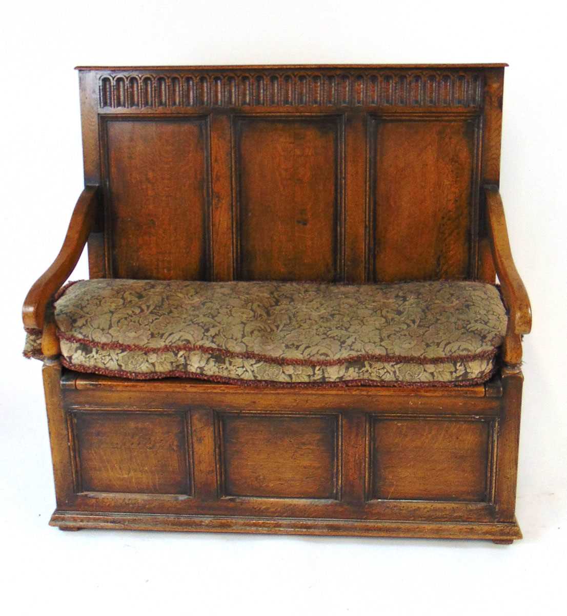 An early 20th century reproduction oak box settle, with a narrow arcaded frieze above three