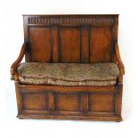 An early 20th century reproduction oak box settle, with a narrow arcaded frieze above three