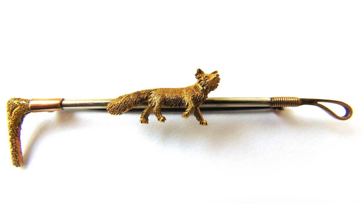 An early 20th century yellow and white metal brooch in the form of a fox and riding crop. Approx.