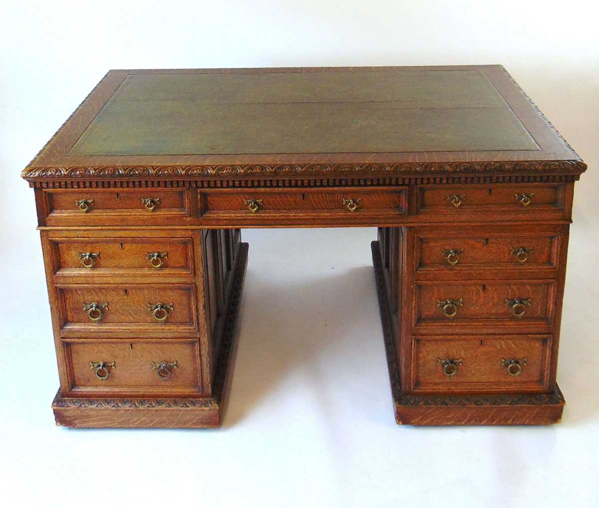 A late Victorian oak partners desk, with green tooled leather writing surface, above a series of