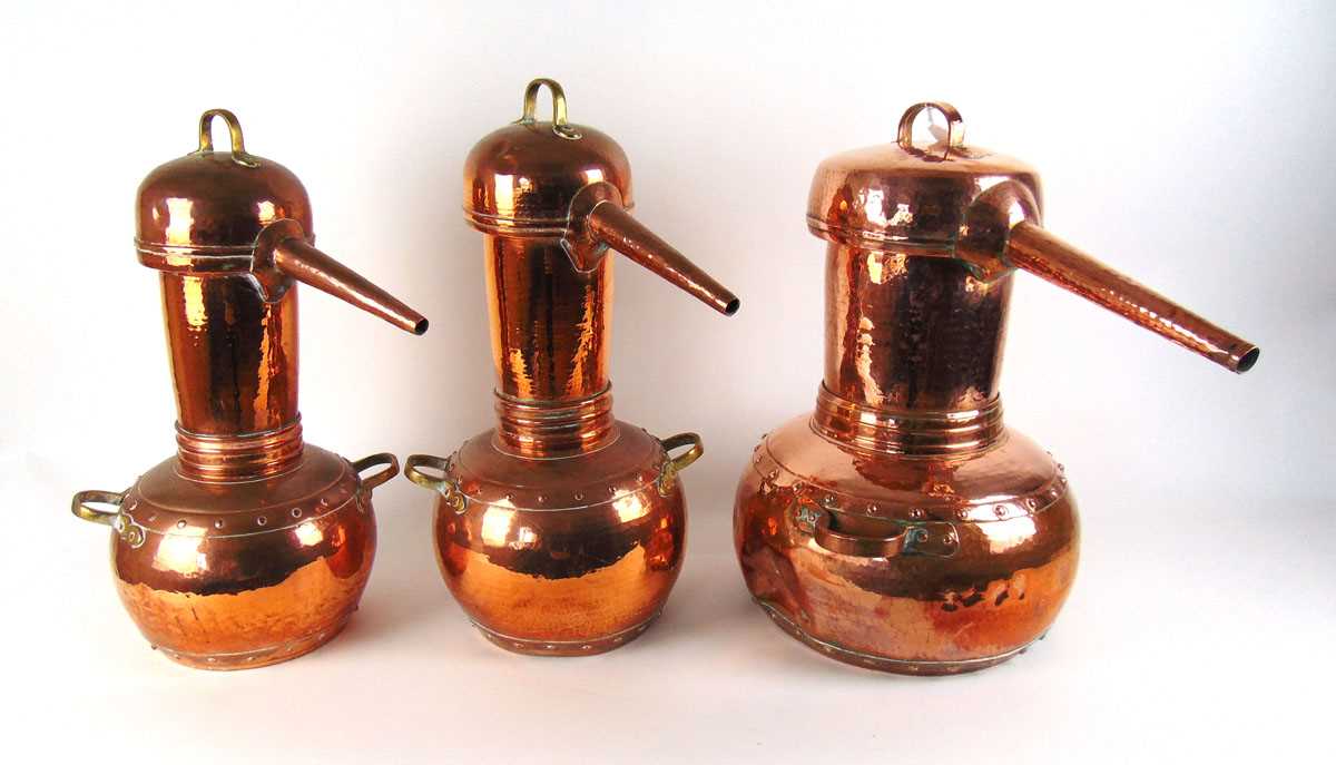 Three copper pot bellied alcohol stills, each with planished decoration, with either brass or copper