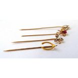 A collection of four yellow metal stick pins to include one in the form of a leaf, wish bone etc.