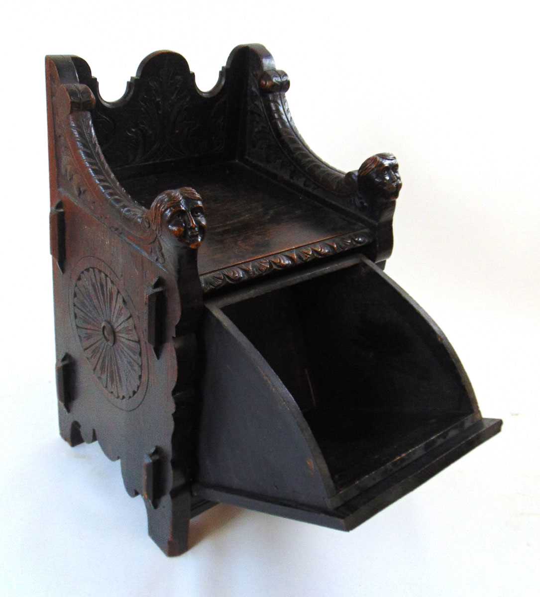 A late Victorian carved and ebonised oak purdonium/seat, decorated with carved masks, foliate