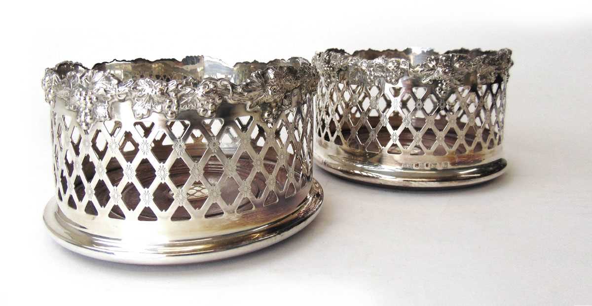 A pair of Elizabeth II silver pierced bottle coasters with turned wooden bases. Hallmarked for