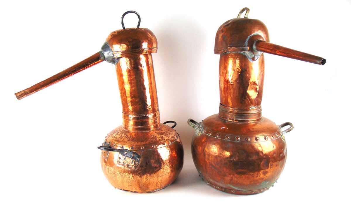 Two large copper pot bellied alcohol stills, each with planished decoration, with either brass or