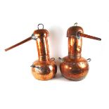 Two large copper pot bellied alcohol stills, each with planished decoration, with either brass or