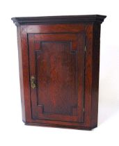 A George III oak wall mounted corner cupboard, with fielded panel door with medullary rays enclosing
