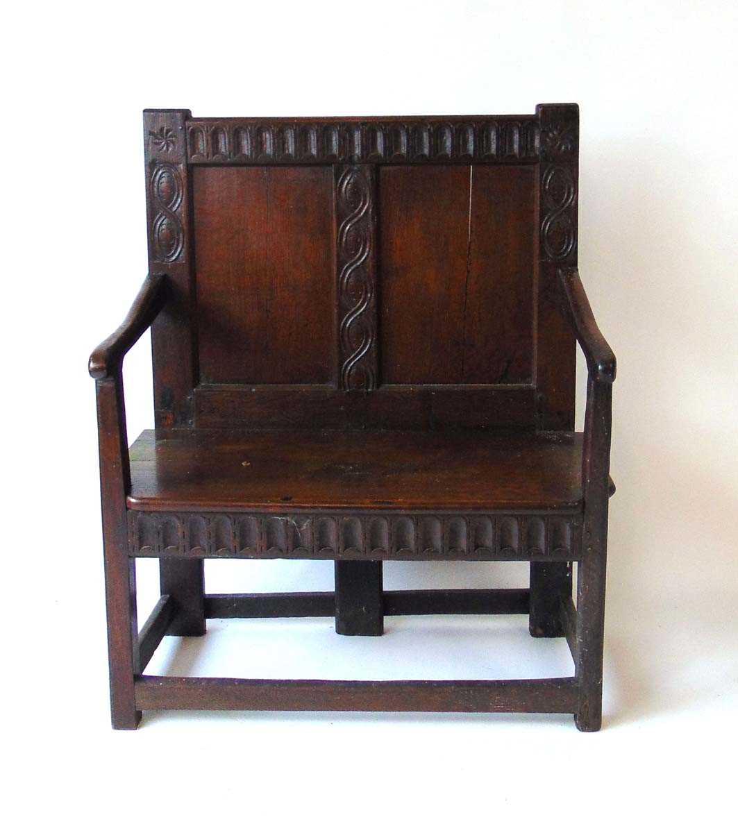 An 18th century and later oak settle, with arcaded top rail flanked by carved wheel and figure of