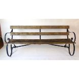 A late Victorian green painted wrought iron and wooden slatted garden bench on scrolled supports,