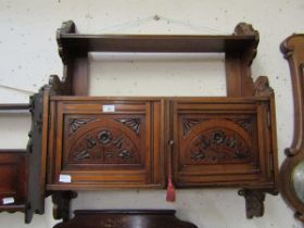 An early 20th century walnut wall mounted cabinet having a pair of carved floral decorated doors