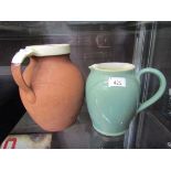 A terracotta jug with cream glazing to top together with a Denby green water jug