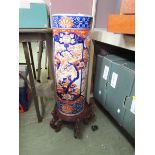 A large oriental ceramic stick stand with naturalistic design on carved wooden base