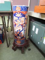 A large oriental ceramic stick stand with naturalistic design on carved wooden base
