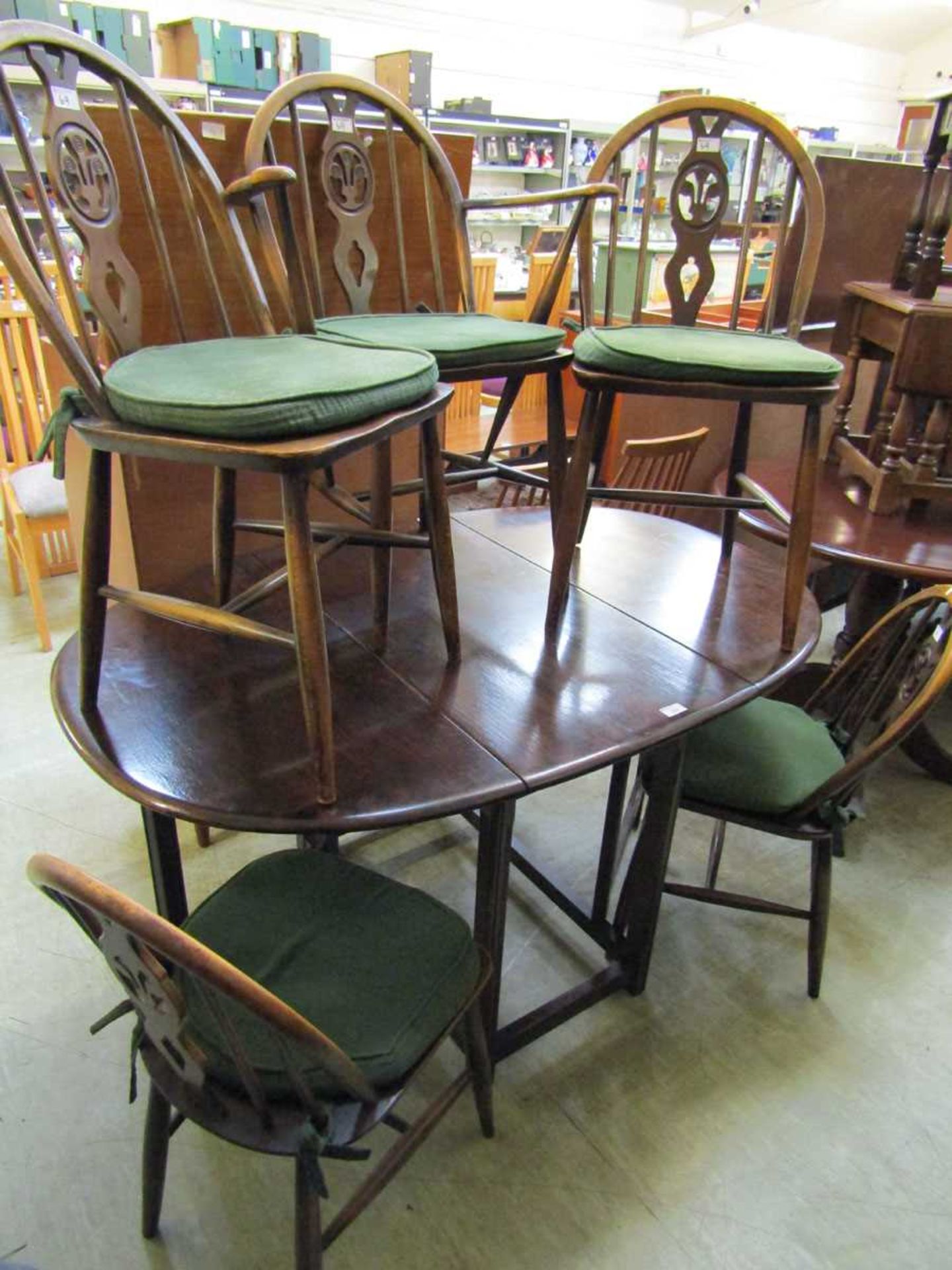 A dark Ercol drop leaf table with a set of four standard wheel back chairs and a single wheel back