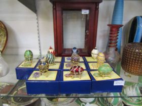 A modern wood and glass display case along with ten boxed 'Atlas Editions' reproduction Faberge eggs